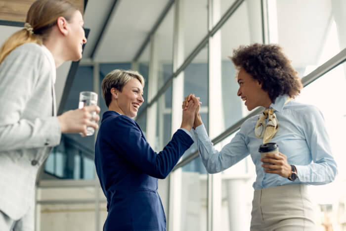 happy businesswomen holding hands while greeting hallway